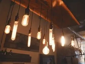 A cluster of illuminated, vintage-style Edison light bulbs of various shapes hanging from a wooden beam.