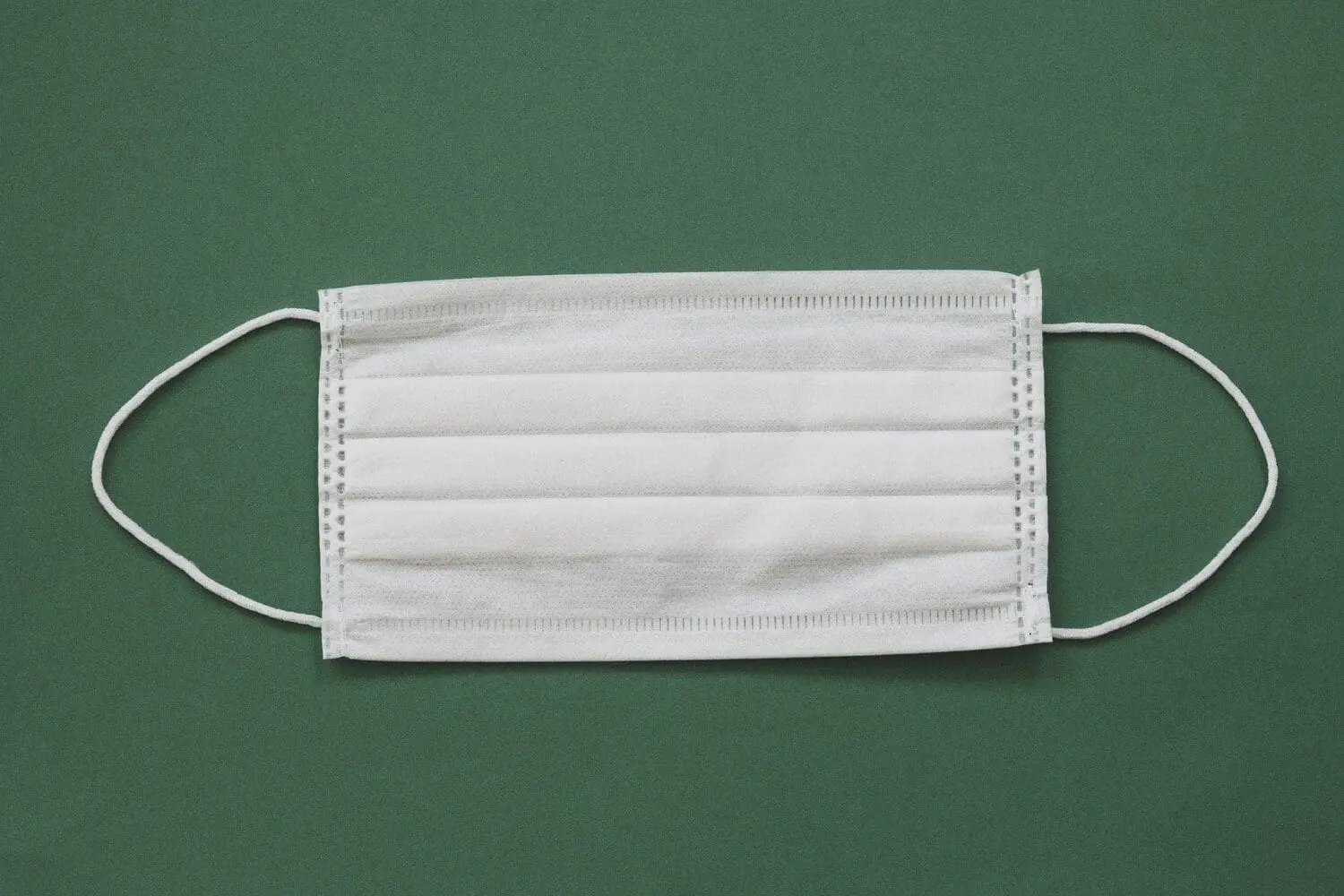 Adherent (formerly Compliance & Risks). A white disposable face mask with ear loops on a dark green background.