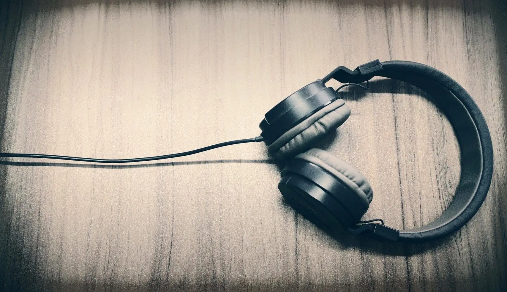 Adherent (formerly Compliance & Risks). Dark over-ear headphones with a cable on a light wooden surface.