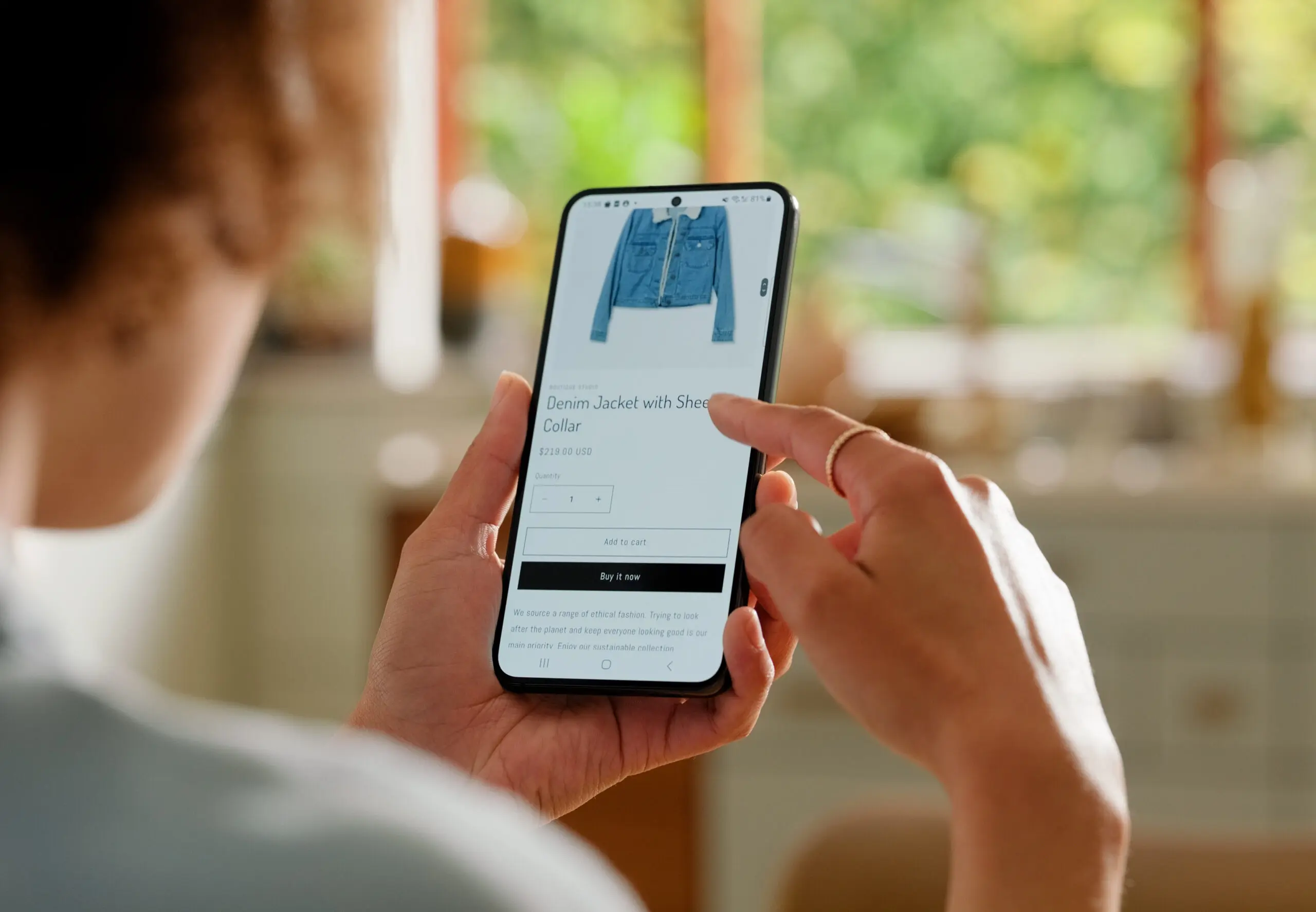 Adherent (formerly Compliance & Risks). A person holds a smartphone displaying an online store page for a denim jacket with a sherpa collar, priced at $219.00 USD. The person's finger is touching the screen.