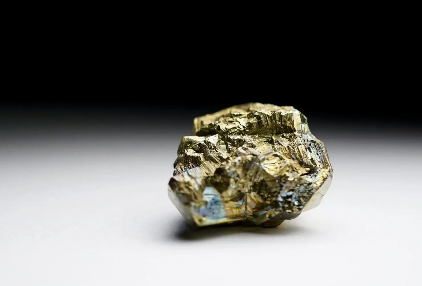 Adherent (formerly Compliance & Risks). A metallic, brassy yellow pyrite mineral specimen with iridescent blue and purple reflections, on a white and black gradient background.