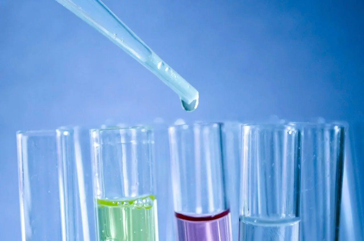 Adherent (formerly Compliance & Risks). A dropper with a suspended drop above test tubes containing green, purple, and clear liquids against a blue background.