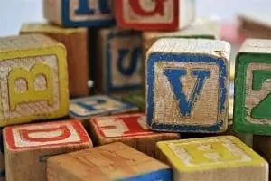 Adherent (formerly Compliance & Risks). Close-up of a pile of worn wooden alphabet blocks with various colored letters like V, B, and D.