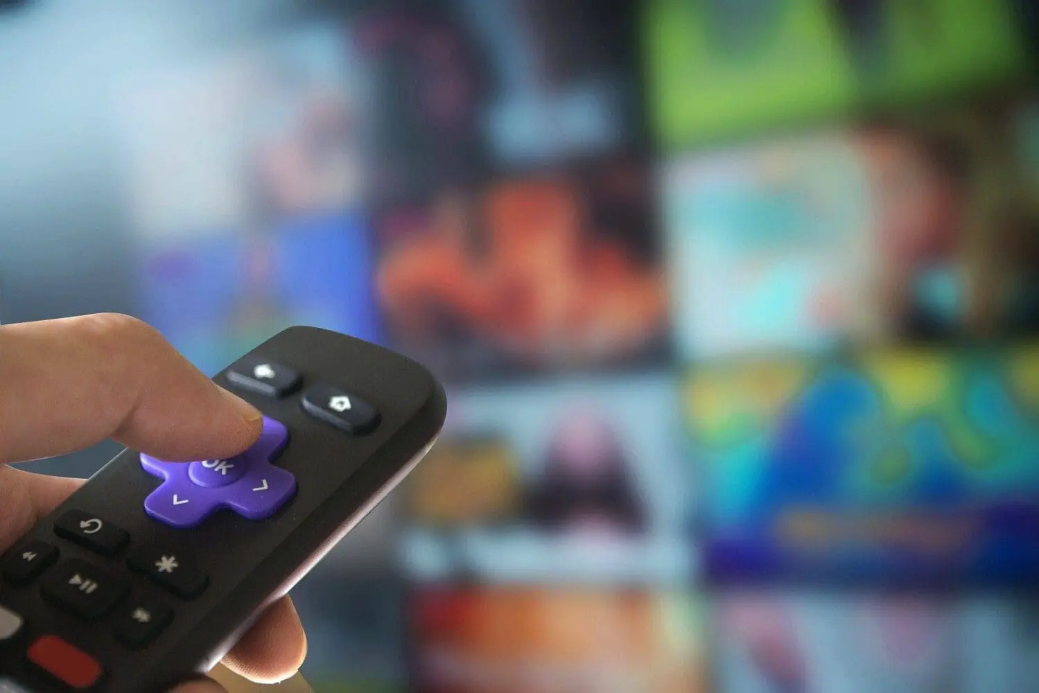 Adherent (formerly Compliance & Risks). A hand holds a black remote control with a purple directional pad, against a blurred background of colorful streaming content thumbnails.