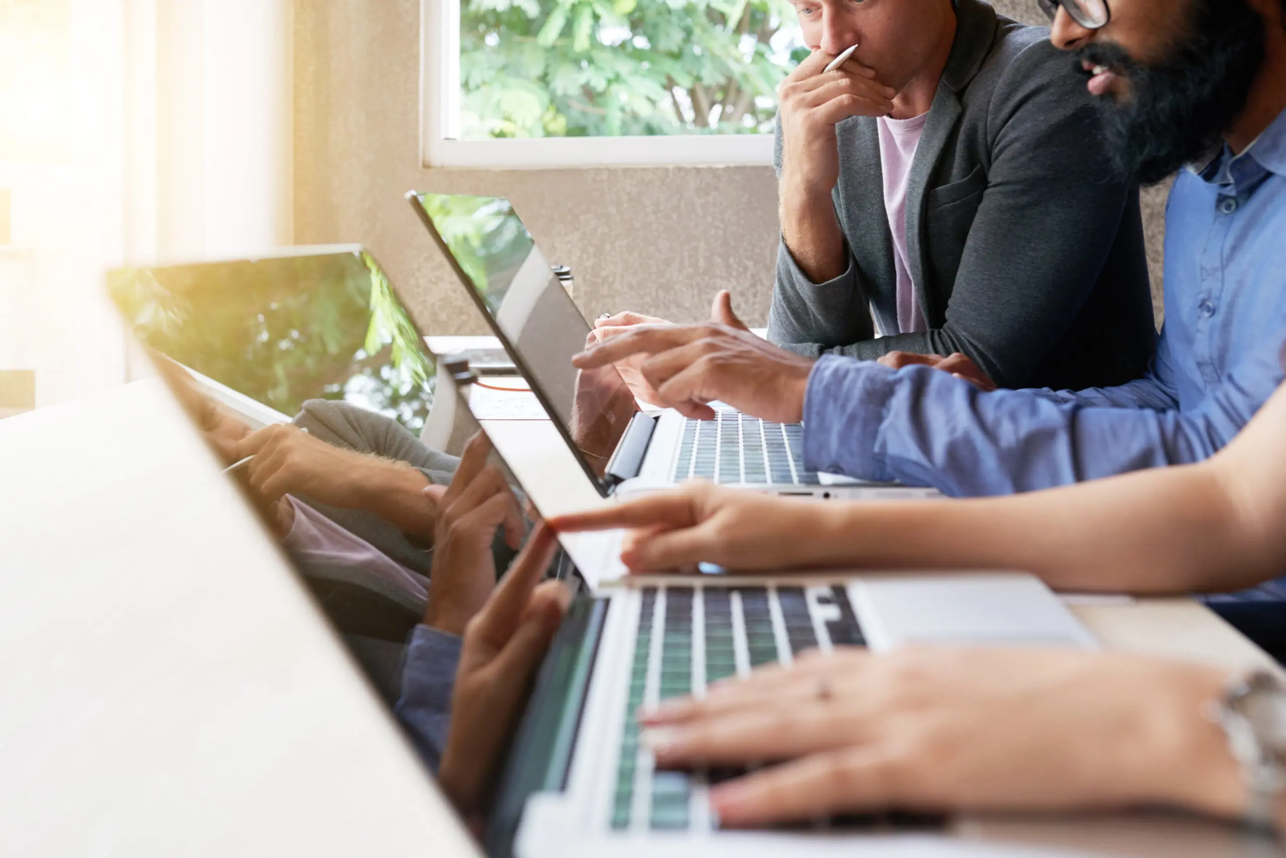 Adherent (formerly Compliance & Risks). Three people working on laptops at a table, one pointing at a screen, with natural light from a window.