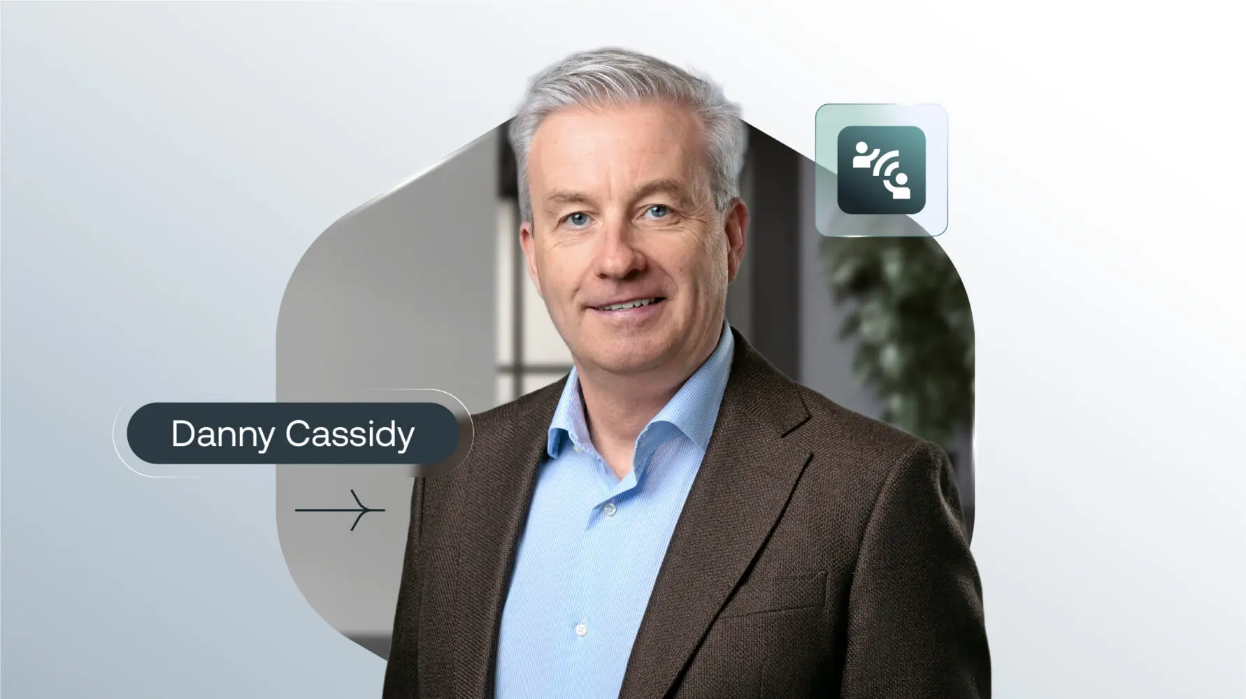 Headshot of Danny Cassidy, a smiling man with grey hair and blue eyes, wearing a blue shirt and brown blazer, against an abstract grey background with his name displayed.