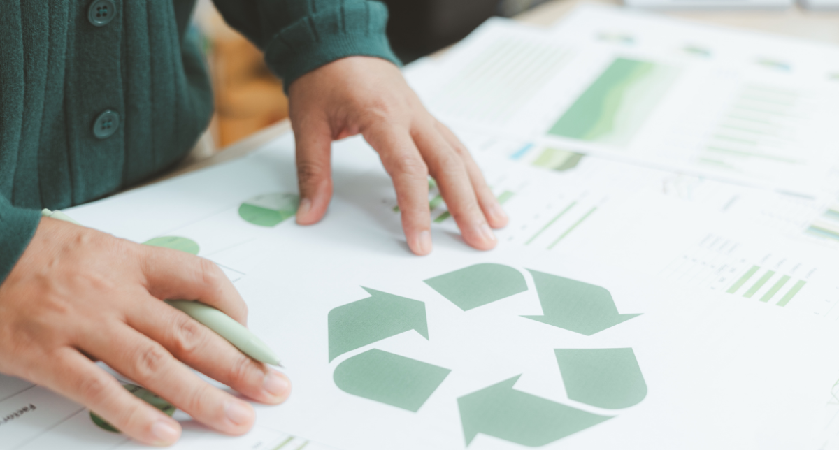 Close-up of hands on papers with green charts, graphs, and a large recycling symbol.