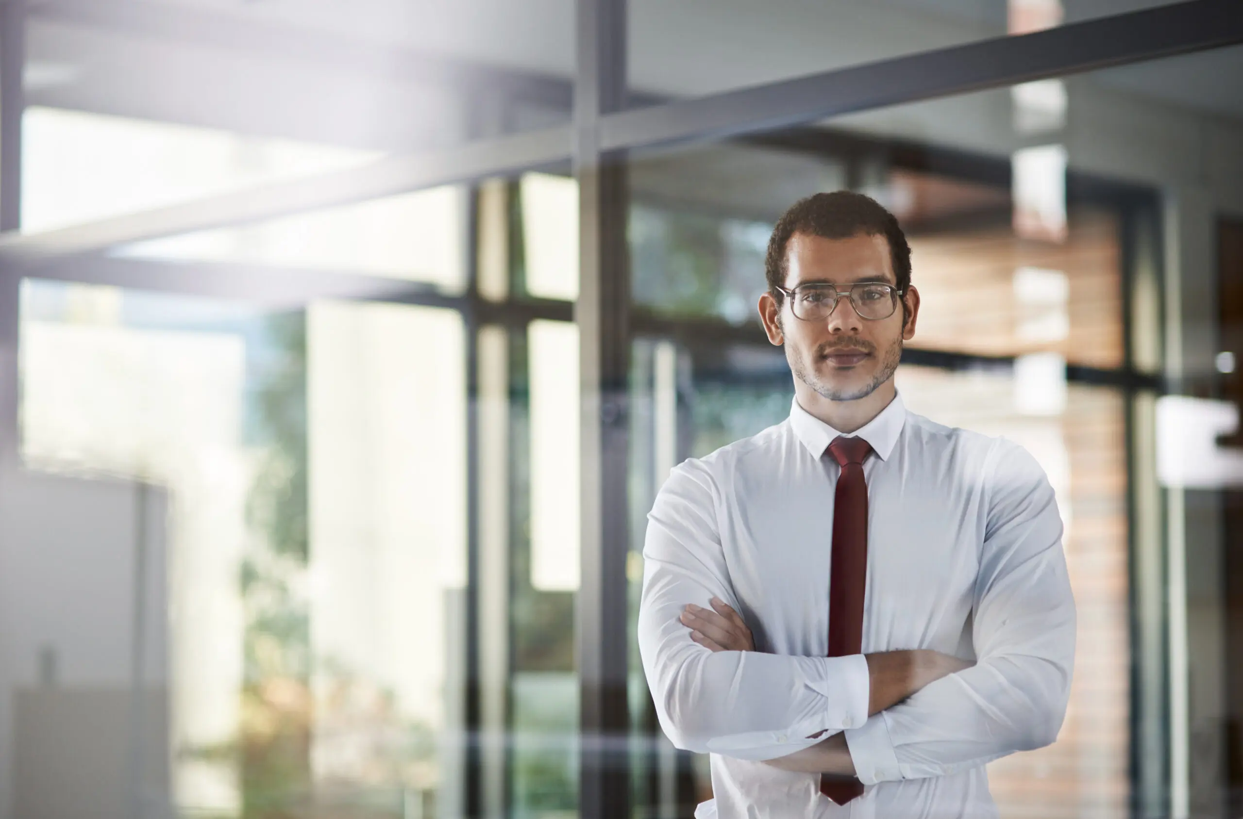 Adherent (formerly Compliance & Risks). A man in a white shirt and red tie with crossed arms looks at the camera in an office.