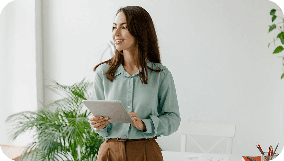 Adherent (formerly Compliance & Risks). A smiling young woman in a light blue shirt and brown pants holds a silver tablet, looking left in a bright room.