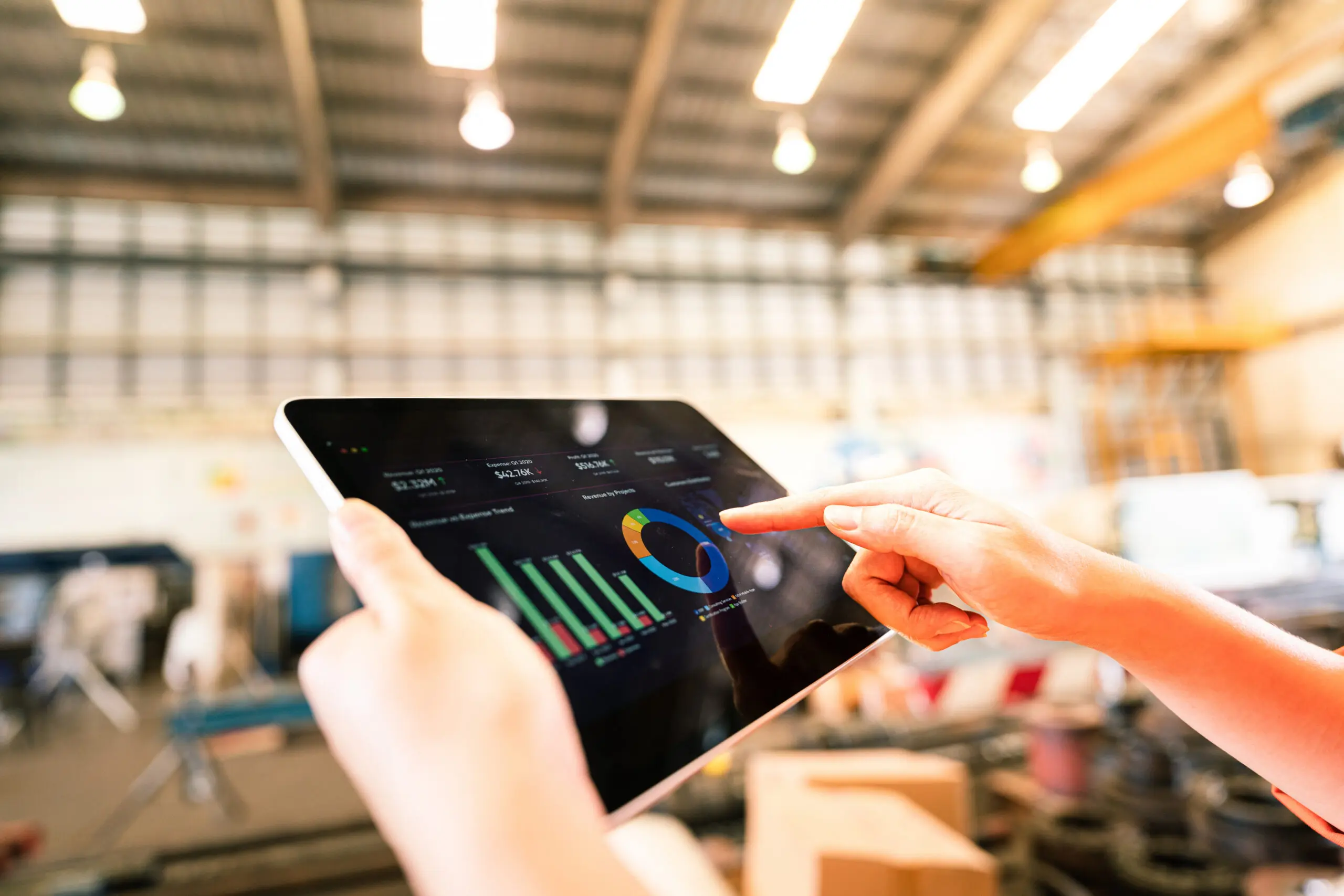 Adherent (formerly Compliance & Risks). Hands holding a tablet displaying financial charts, including bar graphs and a donut chart, in a blurred industrial background.