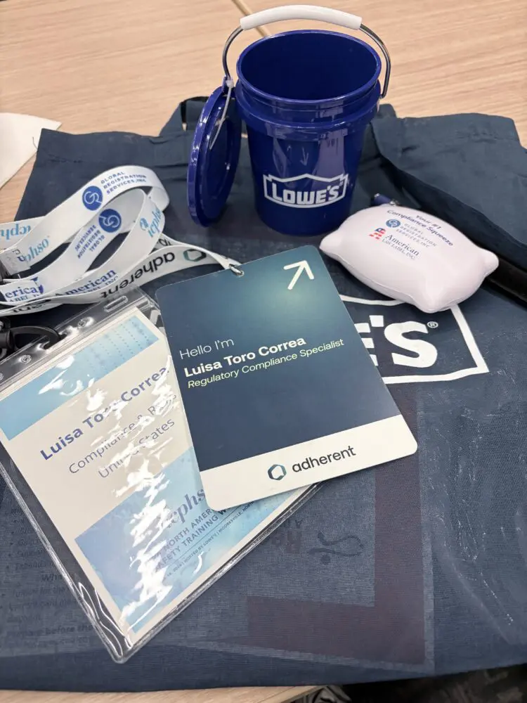 A flat lay of event items: a blue Lowe's bucket, a lemon-shaped stress ball, white lanyards, and an ID badge for Luisa Toro Correa, a Regulatory Compliance Specialist.