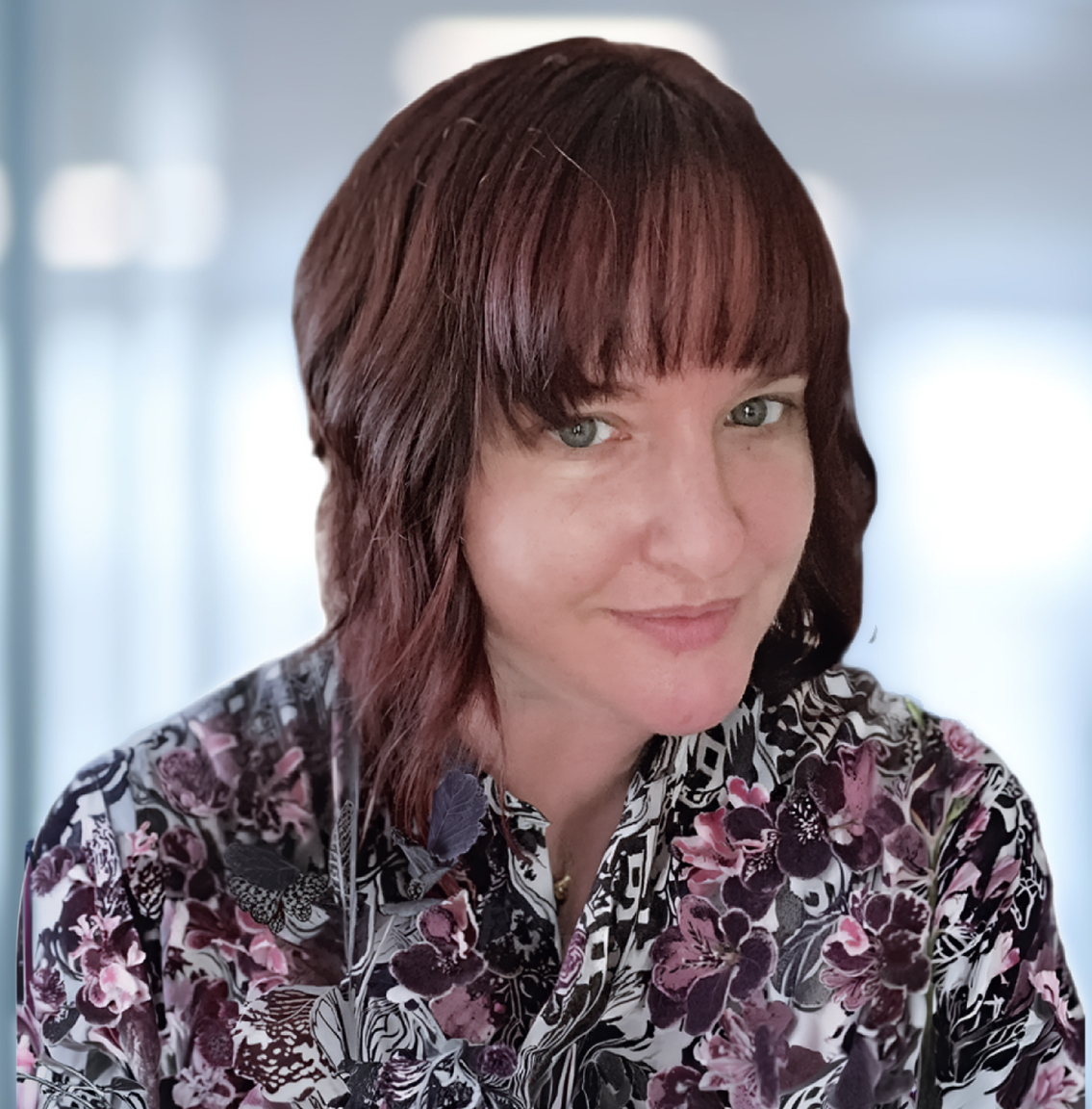 Headshot of a woman with reddish-brown hair, green eyes, and a floral shirt, smiling at the camera.