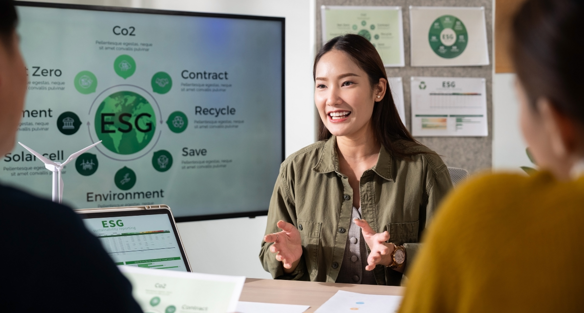 A smiling woman speaks during an ESG meeting, with a screen displaying an ESG diagram and a wind turbine model on the table.