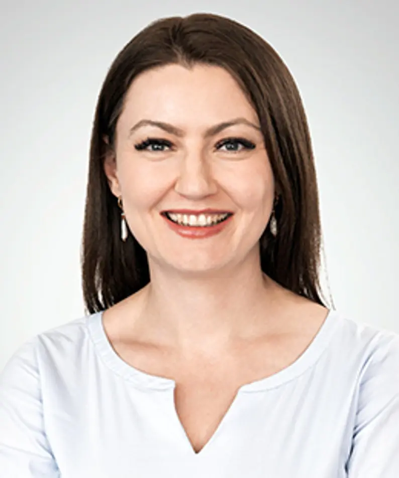 Headshot of a smiling woman with long dark hair and a light blue blouse.