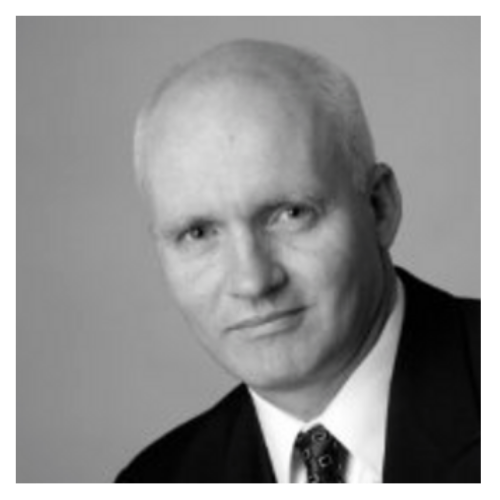 Black and white headshot of a bald man in a dark suit and patterned tie.