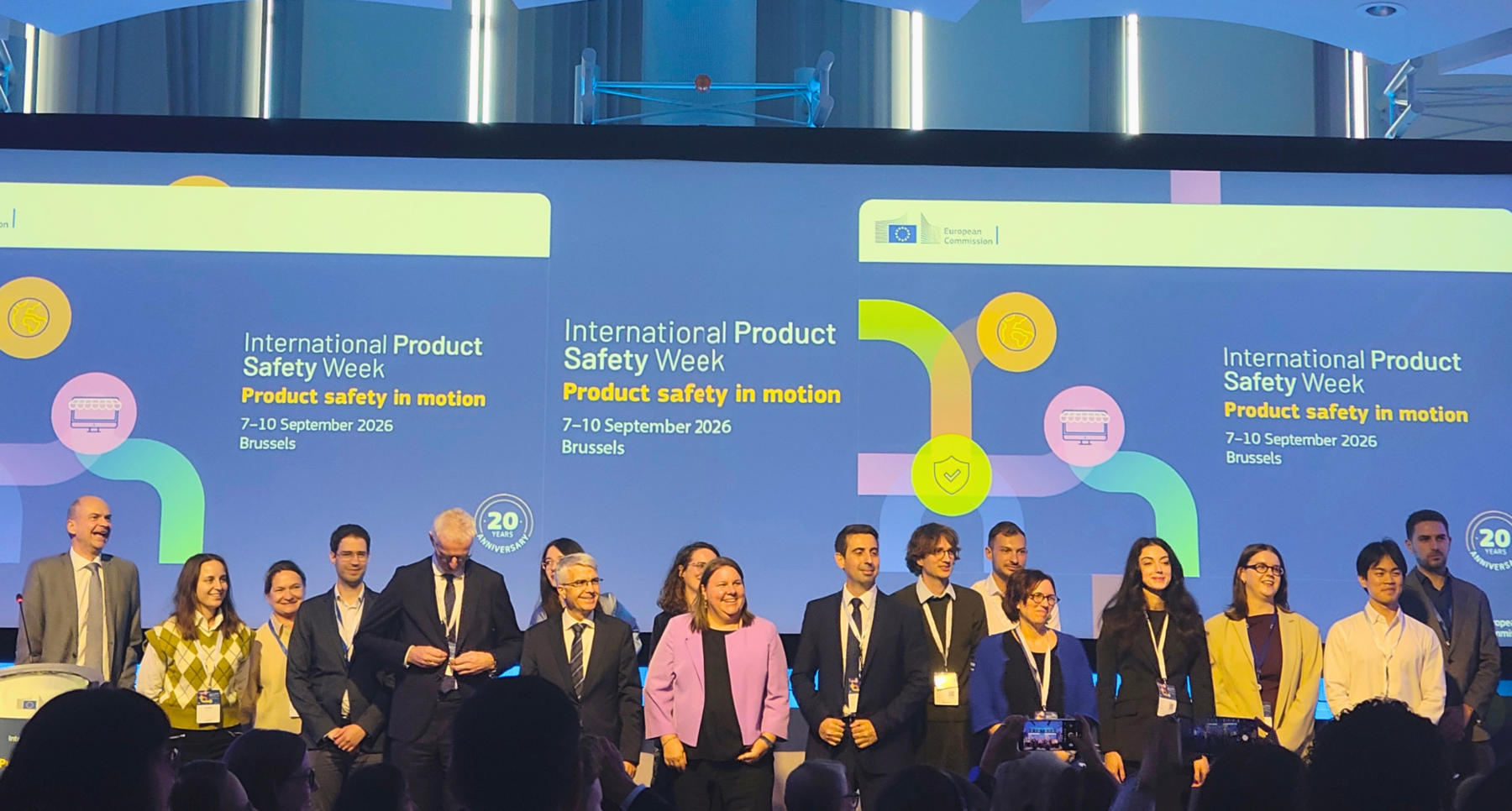 A group of people stands on a stage in front of a large screen displaying 'International Product Safety Week, 7-10 September 2026, Brussels' and the European Commission logo.