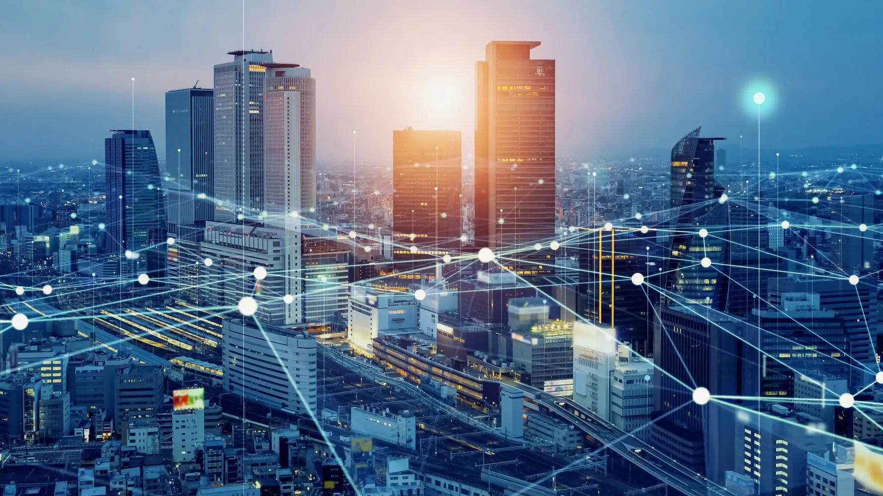 An aerial view of a modern city at dusk with a digital network overlay of glowing lines and nodes connecting buildings and infrastructure.