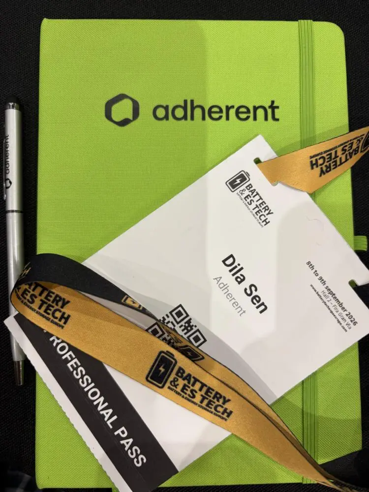 A lime green 'adherent' notebook, a silver 'adherent' pen, and a white 'Battery & ES Tech' conference badge with a gold and black lanyard, showing 'Dila Sen' and 'Professional Pass'.