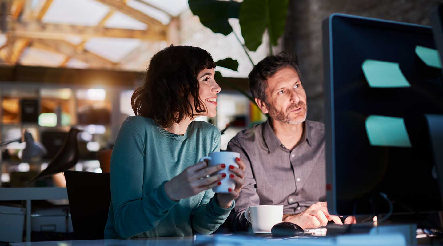 A man and a woman looking at a computer monitor in a dimly lit office.