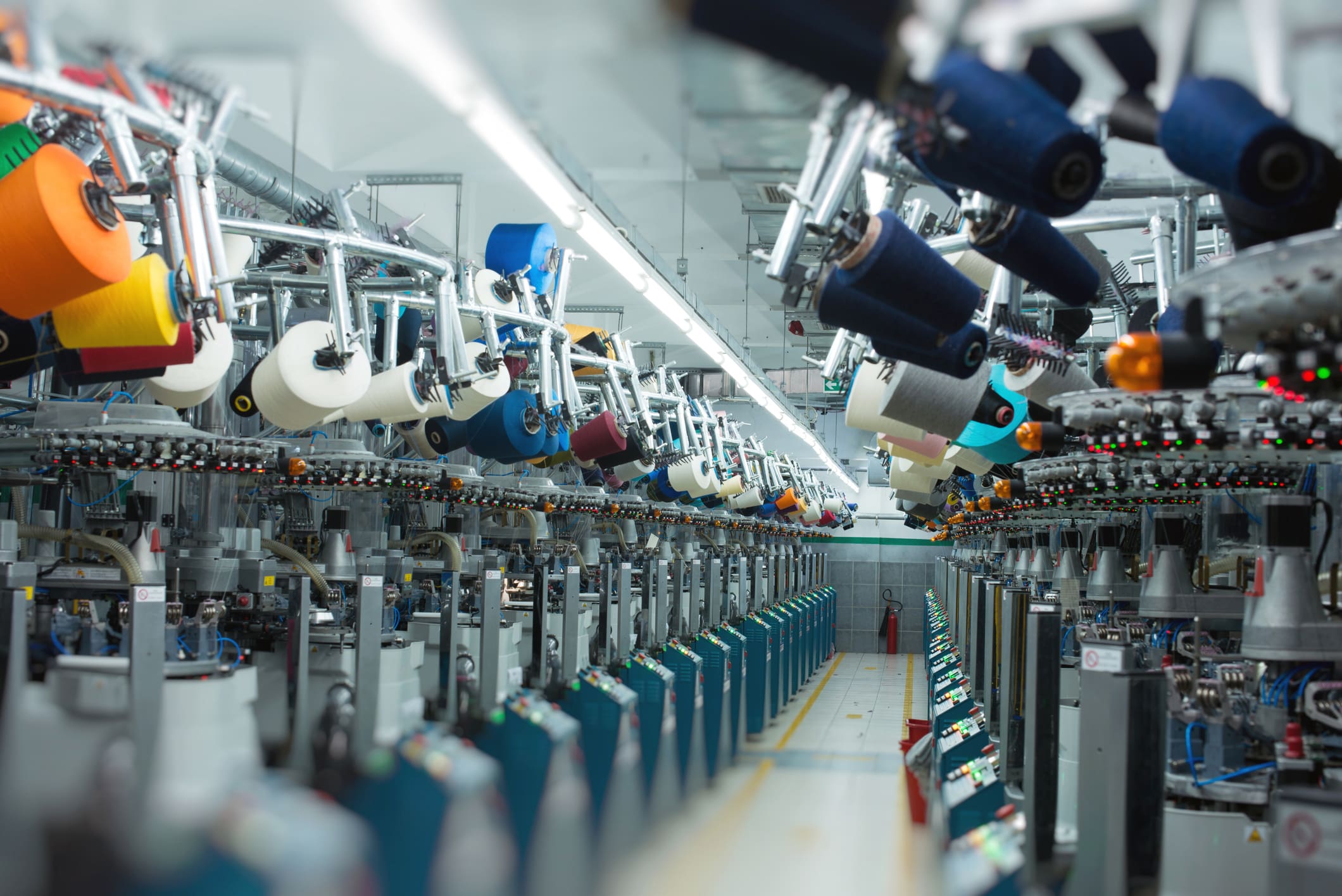 A long view of a textile factory with rows of automated machines, each loaded with numerous colorful yarn spools in various bright colors.