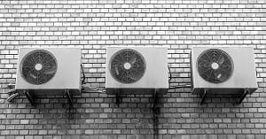Three air conditioning units mounted side-by-side on a brick wall.