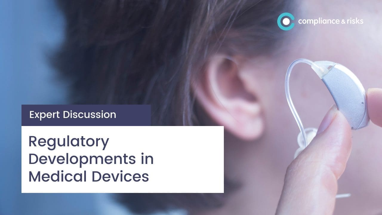 A hand holding a silver hearing aid next to an ear. Text overlay reads 'Expert Discussion' and 'Regulatory Developments in Medical Devices'. A 'compliance & risks' logo is in the top right.
