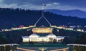 Parliament House in Canberra, Australia, brightly lit at night with a prominent flag mast, viewed from a distance.