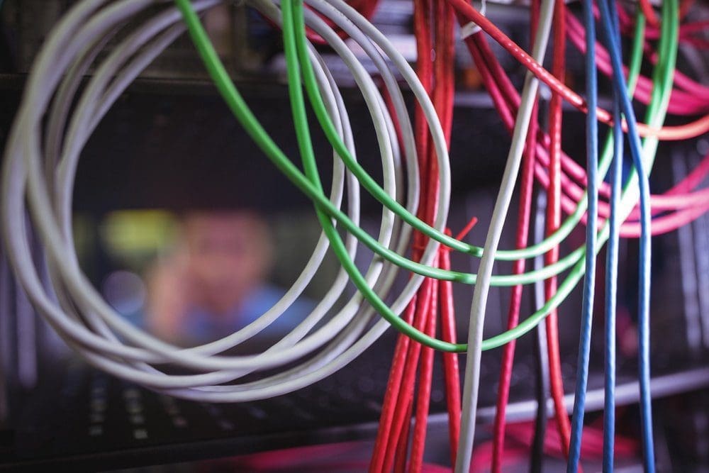 Close-up of numerous colorful network cables, including white, green, red, pink, and blue, in a server environment with a blurred background.