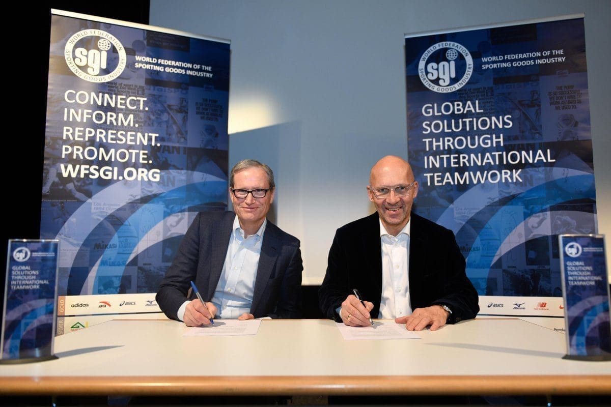Two men, smiling, sign documents at a table with WFSGI banners in the background.