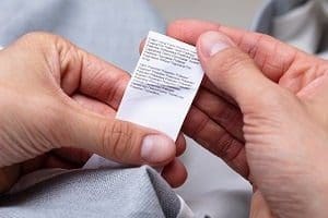 Close-up of hands holding a white clothing care label with small text.