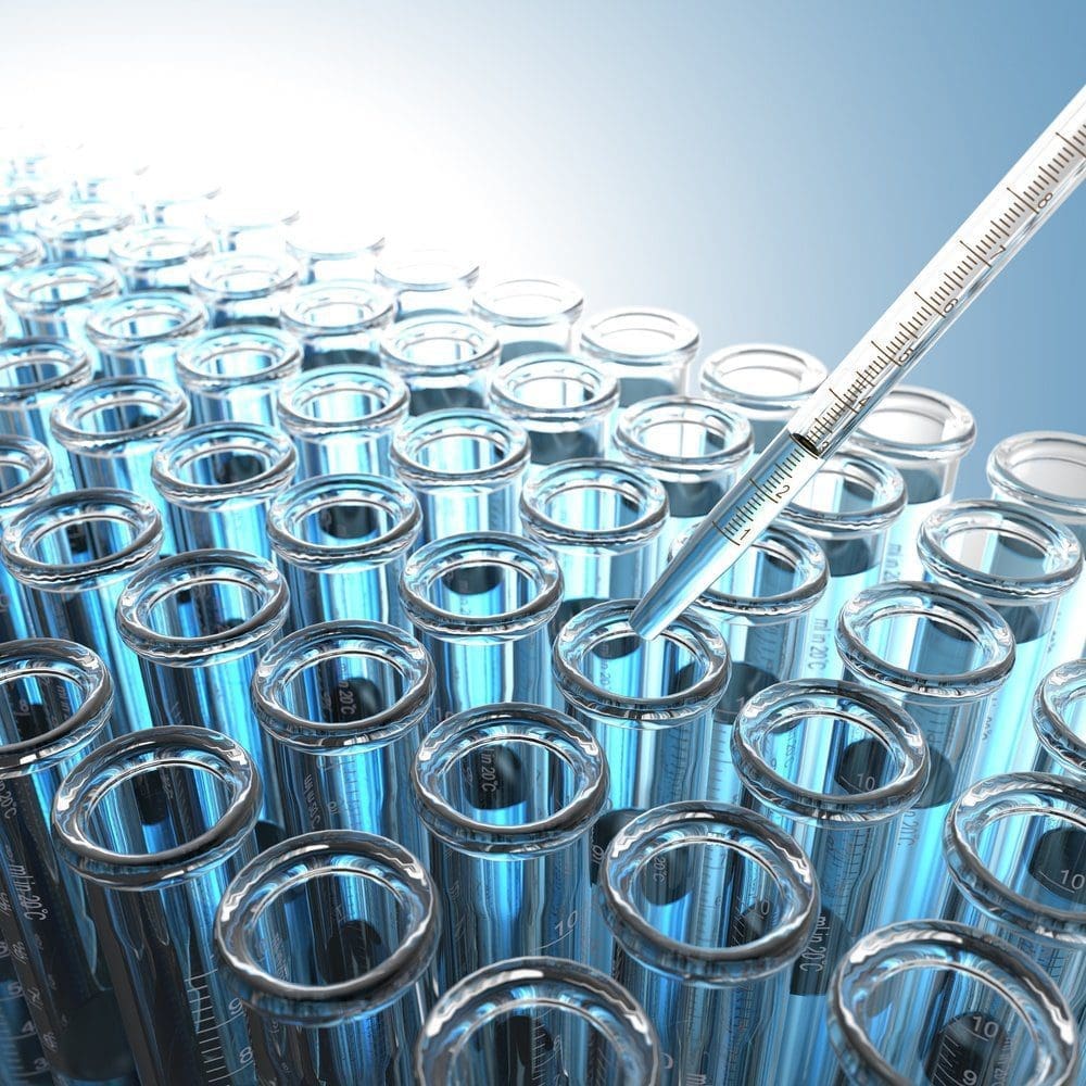 A close-up of many glass test tubes filled with blue liquid, with a pipette dispensing liquid into one of them.