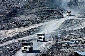 Three large mining trucks on dusty dirt roads in an open-pit mine.