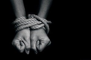 Two hands tied together with rope, clenched into fists, in black and white.