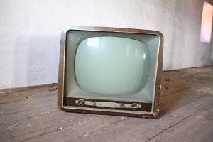An old, vintage television with a dark wooden casing and a curved, light-colored screen sits on a wooden floor.