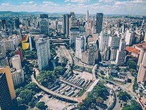 Aerial view of a dense city with numerous tall buildings, roads, and a bus terminal.