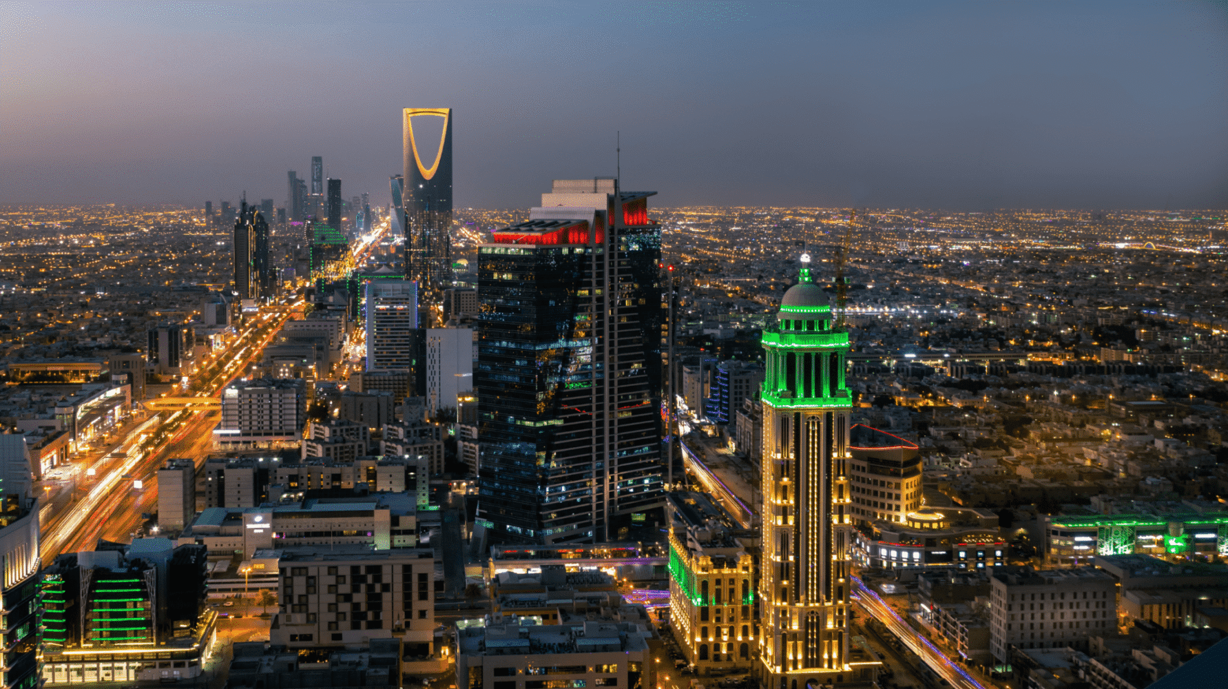 Aerial view of a city at night, showing illuminated skyscrapers, light trails from traffic, and a sprawling urban landscape.