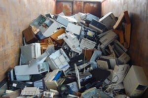 A large pile of discarded computer equipment and electronics inside a rusty metal container.