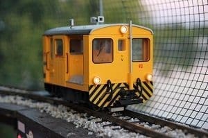A yellow model train car with illuminated headlights on a track, with a blurry background.