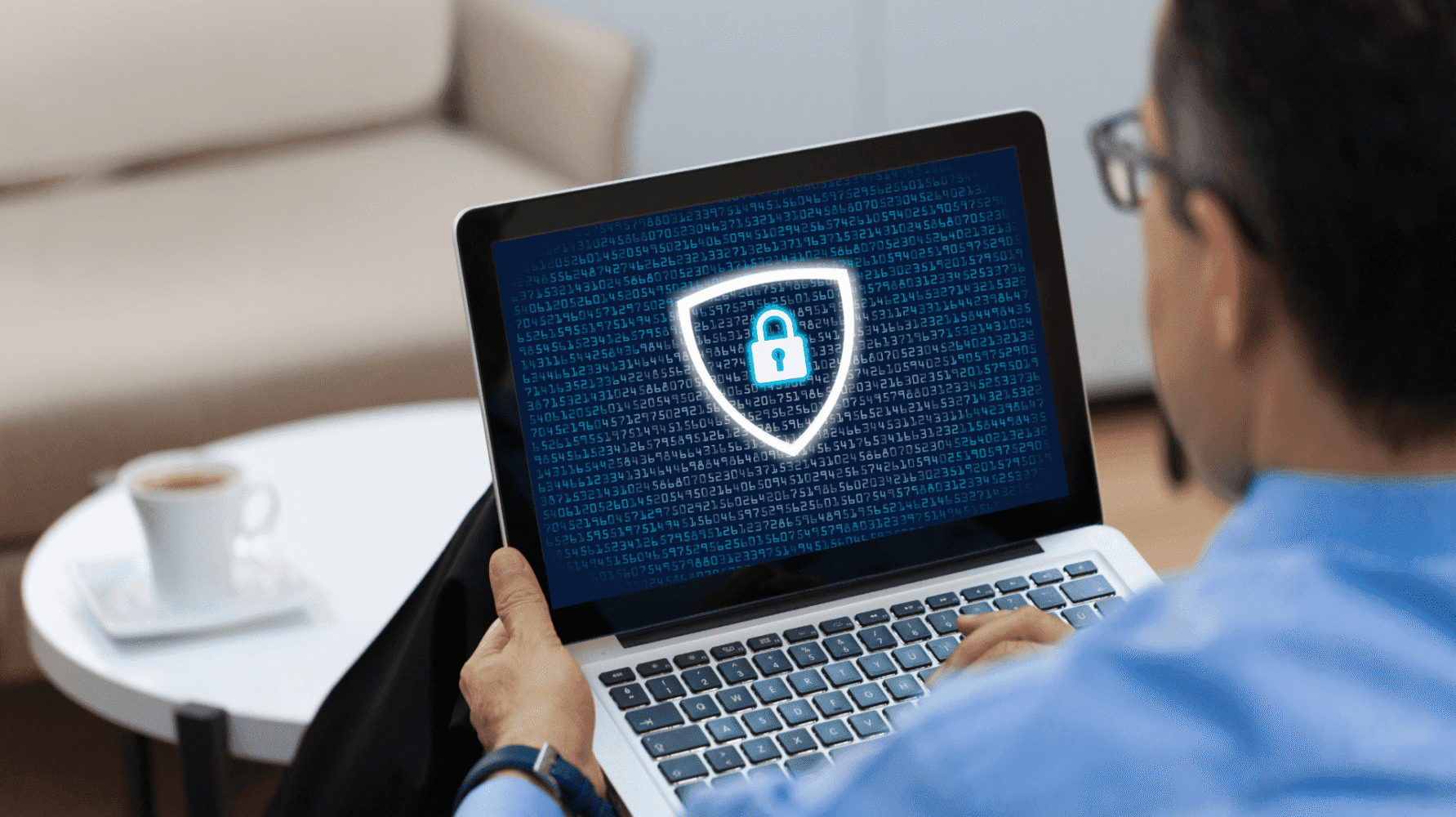 A man typing on a laptop, with a digital security shield and padlock icon displayed on the screen over lines of code.
