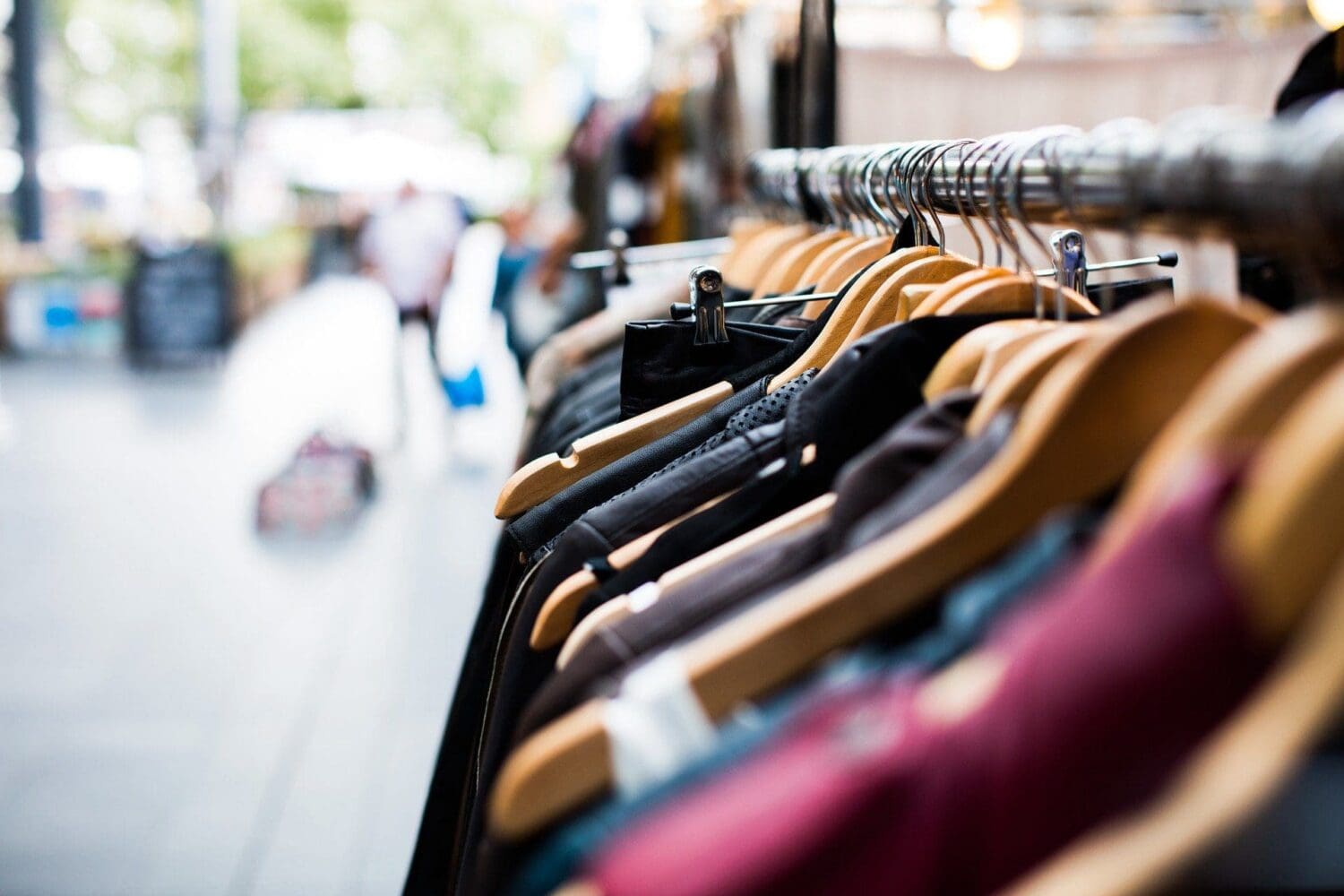 Close-up of a clothing rack with various garments on wooden hangers, against a blurred outdoor background.