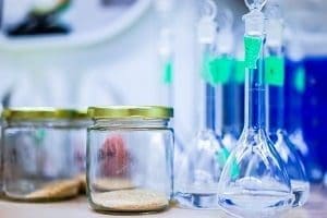 Two glass jars with granular material and several laboratory flasks with clear and blue liquids.