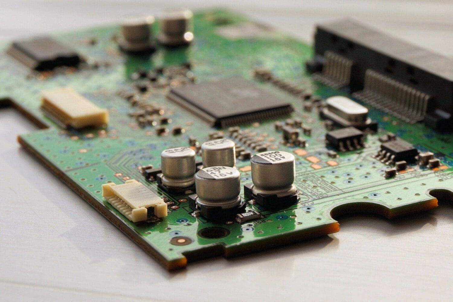 Close-up of a green circuit board with silver capacitors, a large square chip, and various other electronic components.