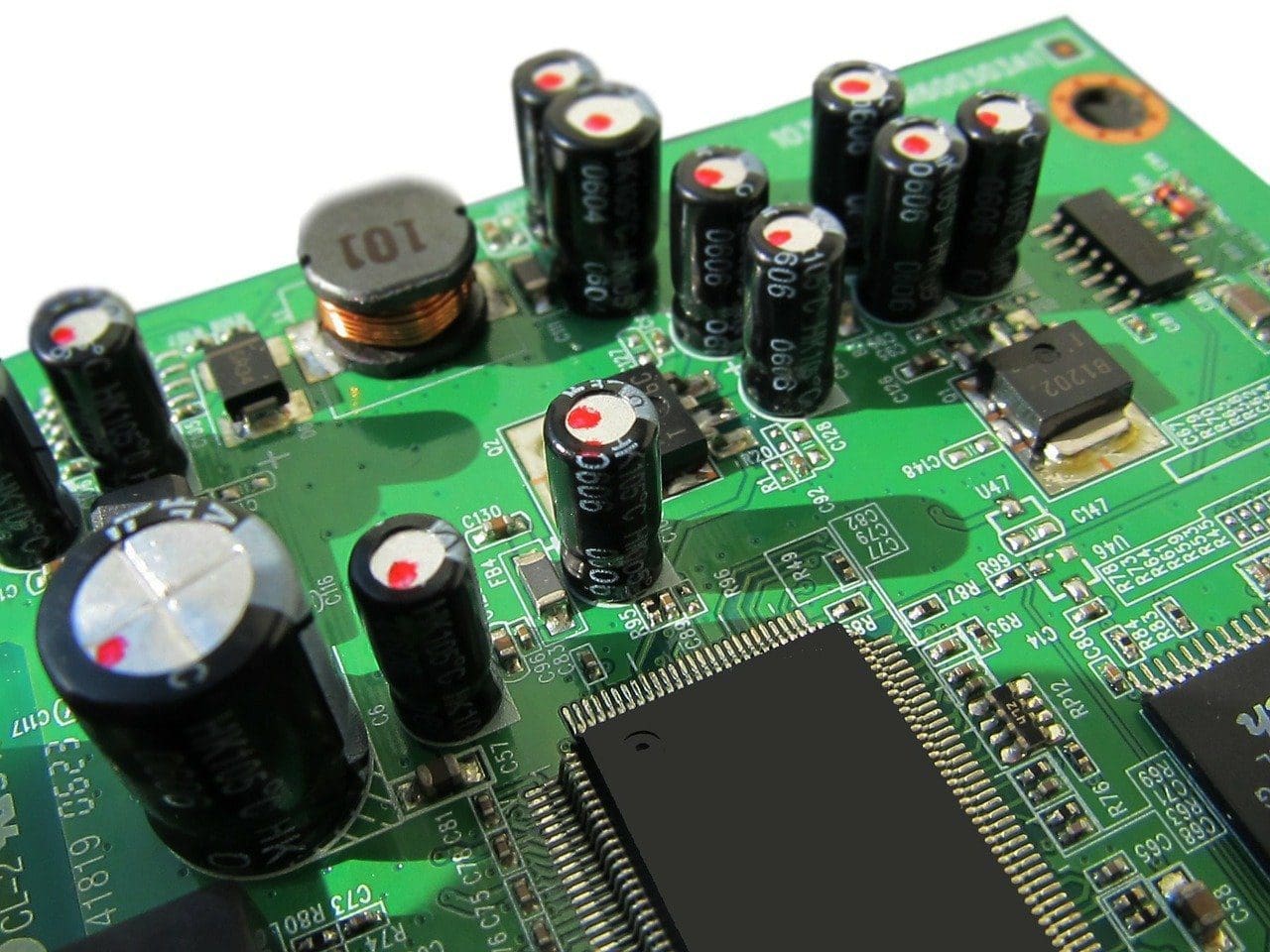 Close-up of a green circuit board with black capacitors, integrated circuits, and an inductor.