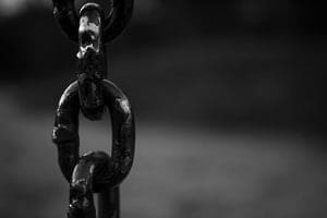 Close-up of two heavy, dark metal chain links in black and white, with a blurred background.