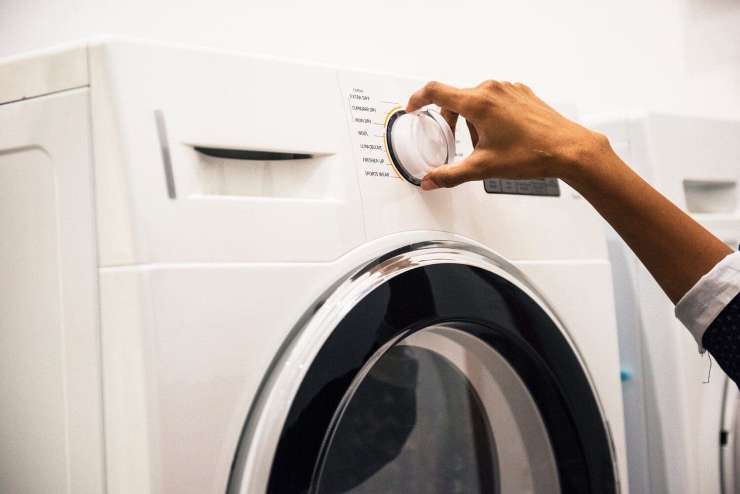 A person's hand turns a clear dial on a white washing machine or dryer, selecting a cycle.