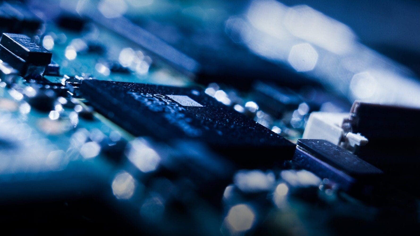 Close-up of a circuit board with a dark microchip in focus, surrounded by blurred blue and white lights.