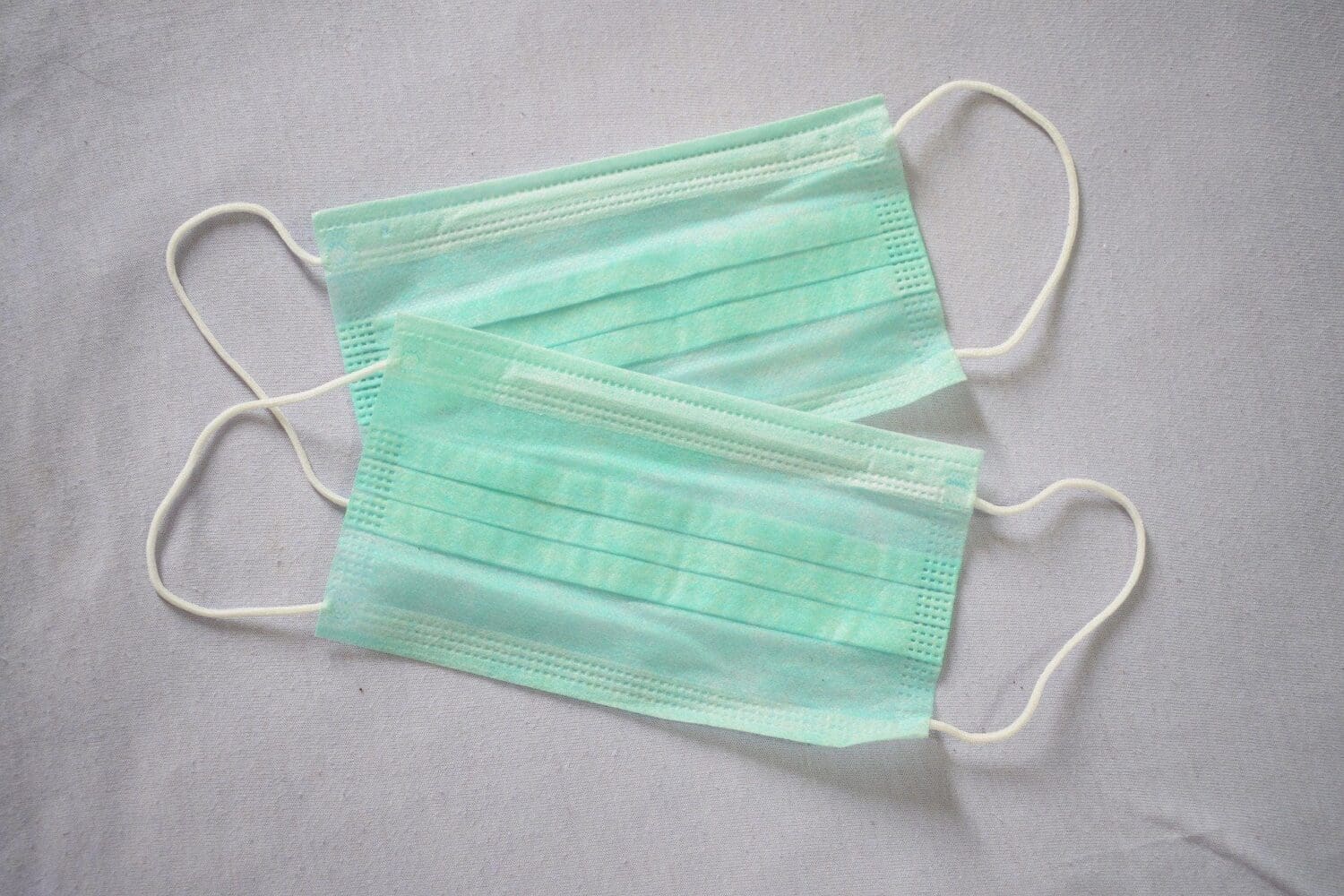 Two light green disposable surgical masks on a grey background.