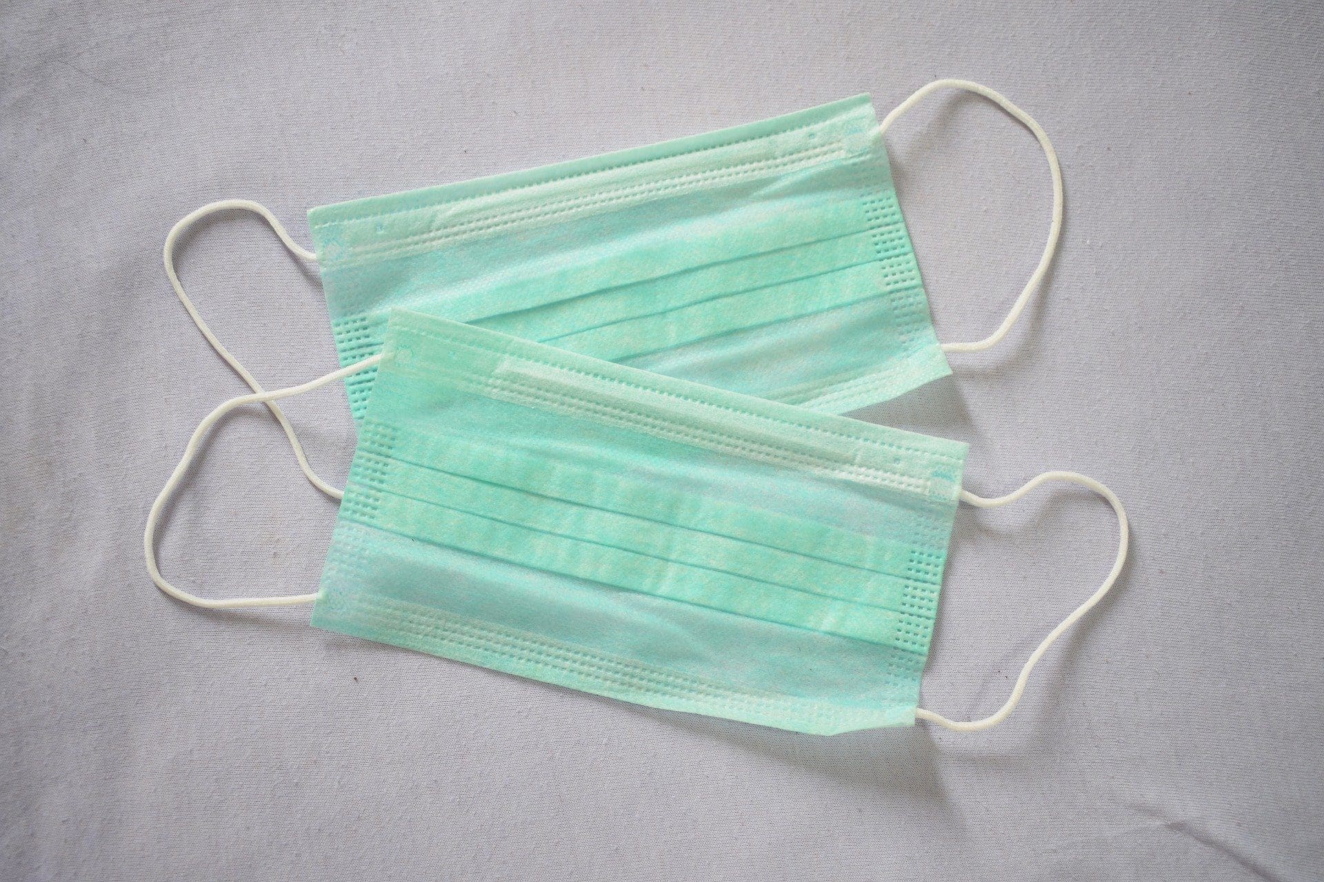 Two light green disposable surgical masks on a grey background.