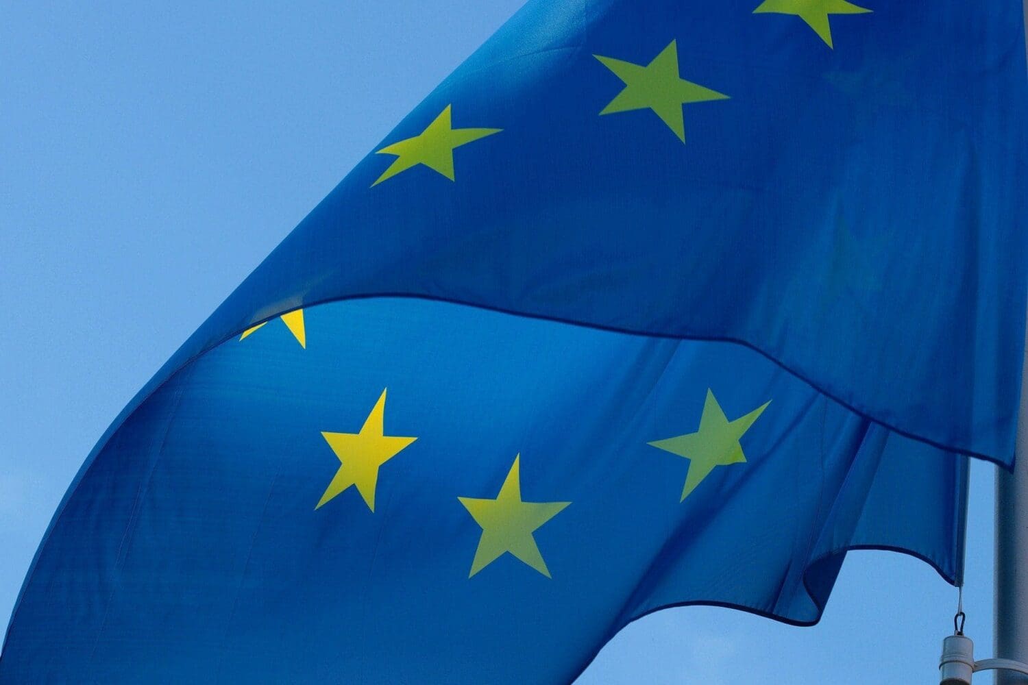 The blue flag of the European Union with yellow stars, waving against a clear blue sky.