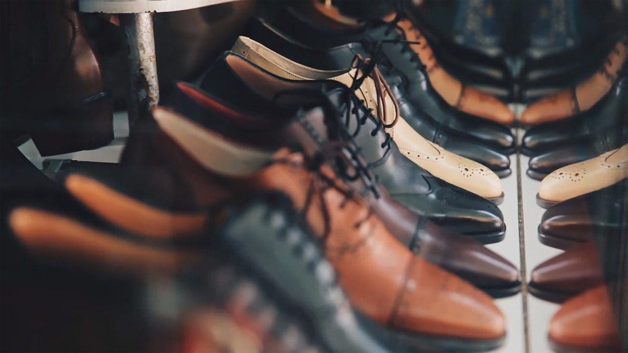 Rows of black, brown, and beige leather dress shoes with brogue detailing, reflected in a mirror.